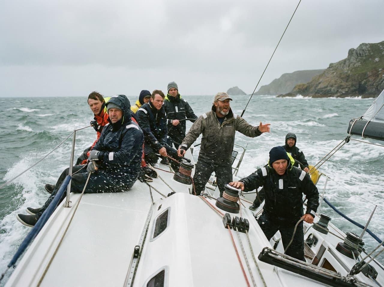 Crew working a yacht together in heavy coastal weather — teamwork under real pressure